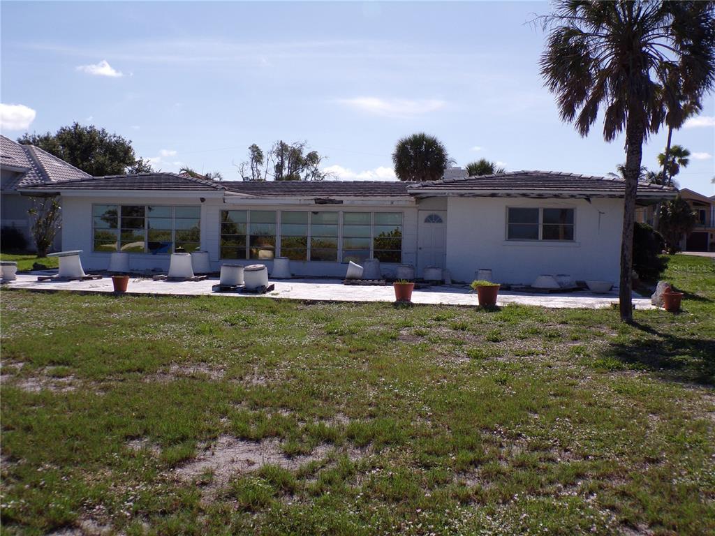 The rear exterior of a single-story house features a large patio with numerous potted plants — 1124 SUNSET DRIVE, VENICE, FL