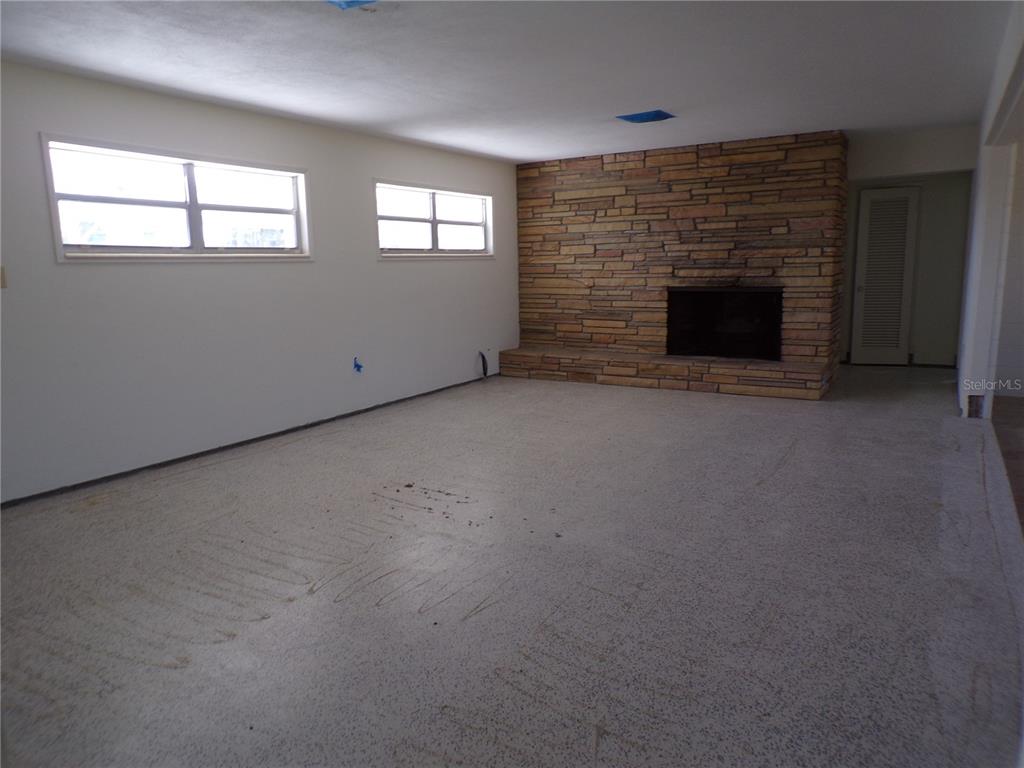An empty living room features a stone fireplace, white walls, and a concrete floor — 1124 SUNSET DRIVE, VENICE, FL
