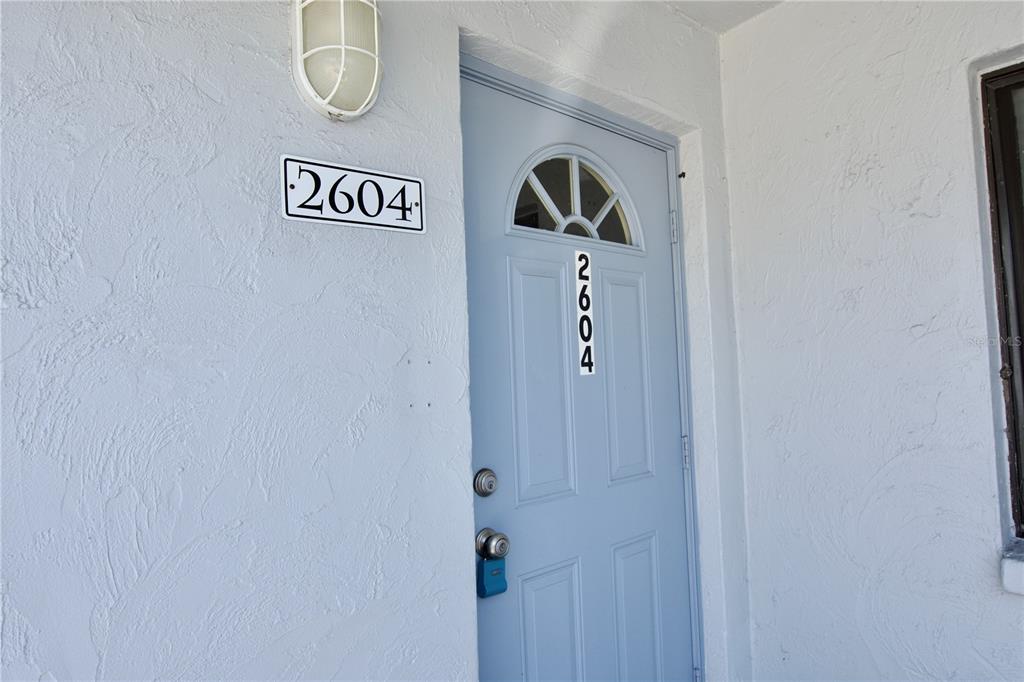 A light blue front door with a small window and house numbers sits on a wall — 5310 26TH STREET W UNIT 2604, BRADENTON, FL