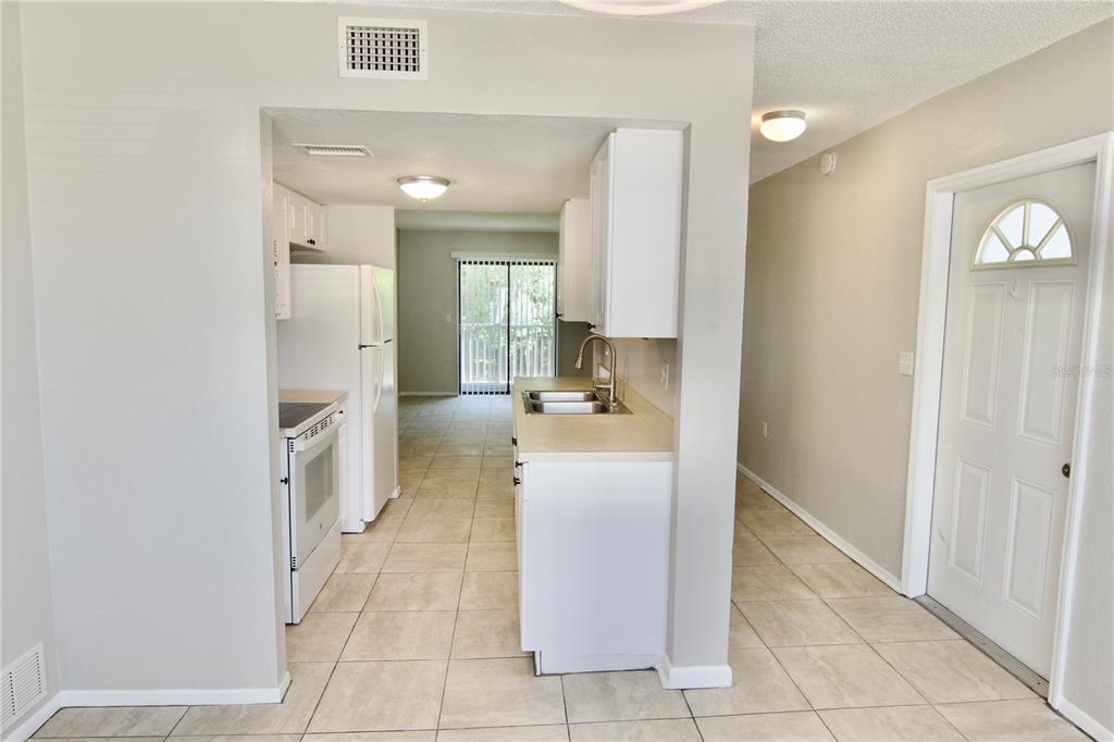 A kitchen with white cabinets, tile floors, and a white refrigerator opens to a balcony — 5310 26TH STREET W UNIT 2604, BRADENTON, FL