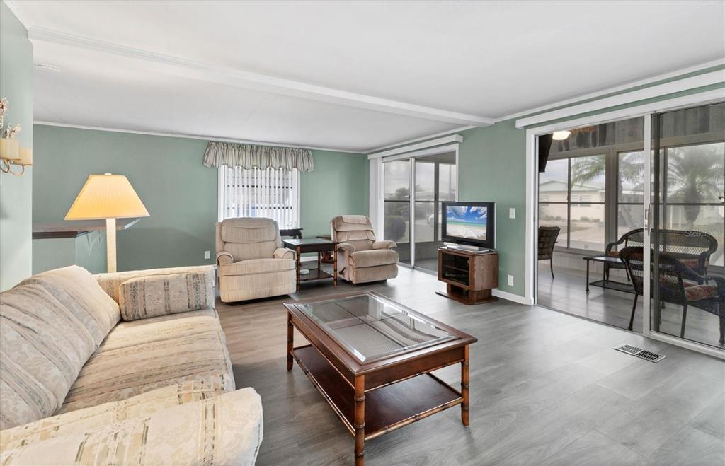 A living room with light green walls, wood-look flooring, a glass-top coffee table, and sliding doors — 1212 45TH AVENUE E, ELLENTON, FL