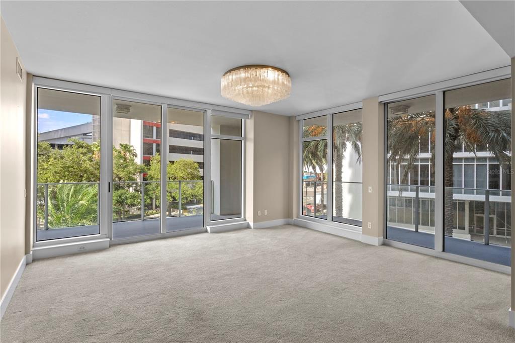 An empty room with beige carpet, a crystal chandelier, and floor-to-ceiling windows overlooking a balcony — 175 1ST STREET S UNIT 303, ST PETERSBURG, FL