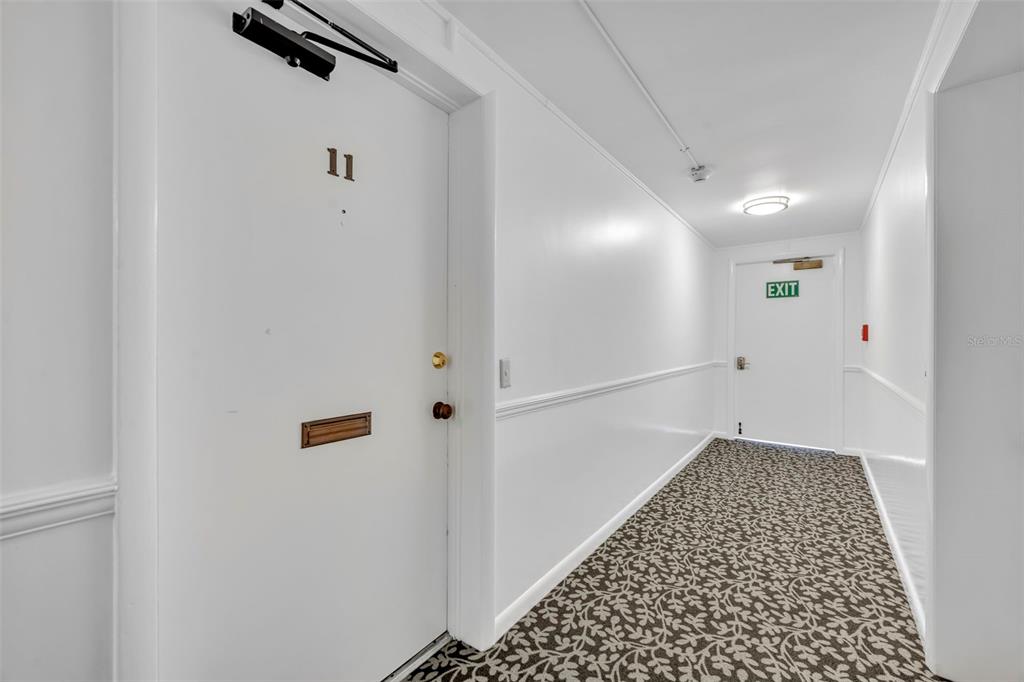 A white hallway features a door labeled 11, patterned carpeting, and an exit door — 311 E MORSE BOULEVARD UNIT 7-11, WINTER PARK, FL