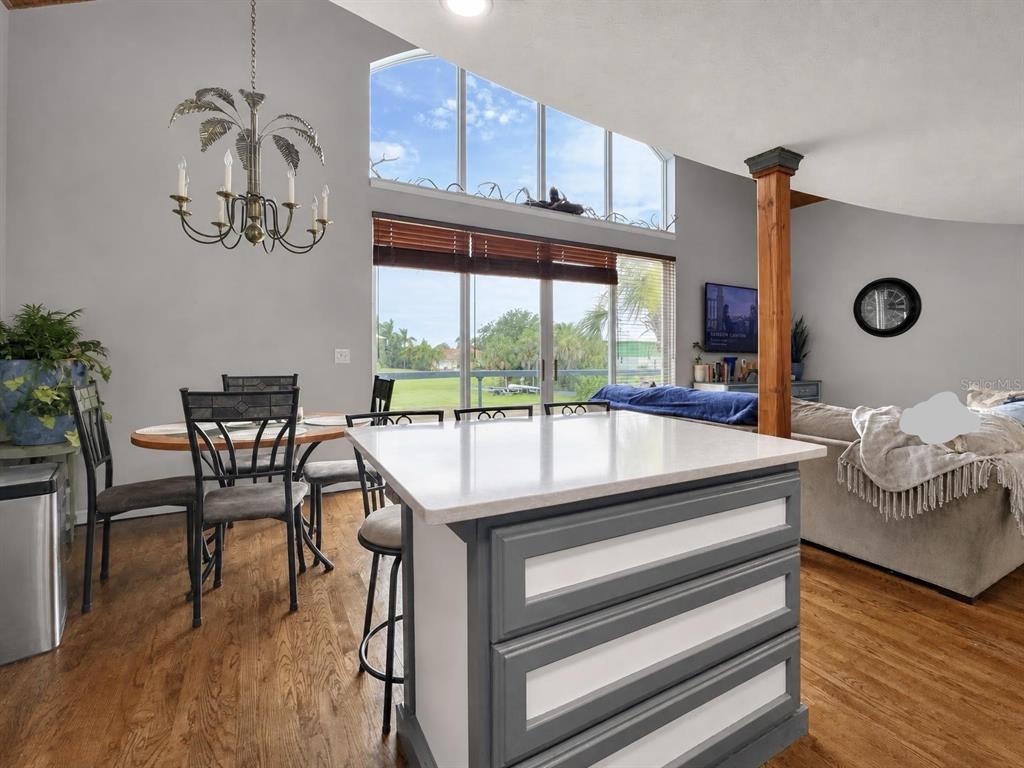 A kitchen island with gray and white cabinetry sits before a dining area and living room — 155 DANFORTH DR, PUNTA GORDA, FL