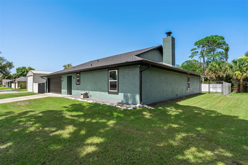 A side view of a single-story house with green stucco siding, a chimney, and lawn — 2817 YULE TREE DRIVE, EDGEWATER, FL
