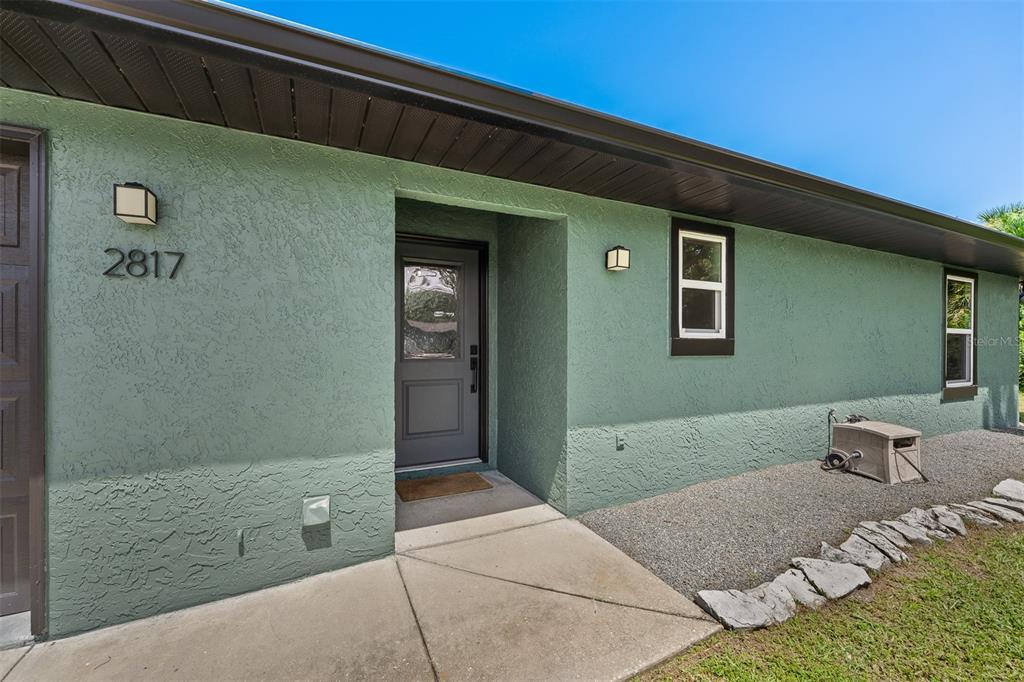A green stucco house exterior features a dark front door and two rectangular windows — 2817 YULE TREE DRIVE, EDGEWATER, FL