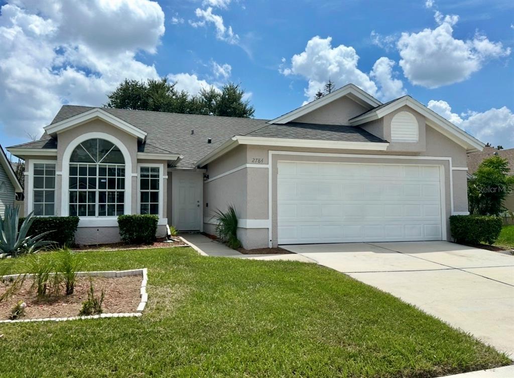A single-story house with a beige stucco exterior, a two-car garage, and a front lawn — 2784 FALLING TREE CIRCLE, ORLANDO, FL