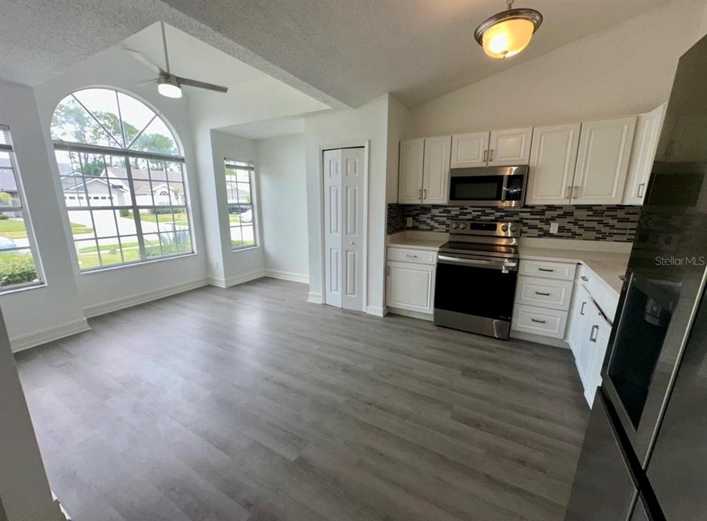 A kitchen with white cabinets, stainless steel appliances, and wood-look flooring next to a dining area — 2784 FALLING TREE CIRCLE, ORLANDO, FL