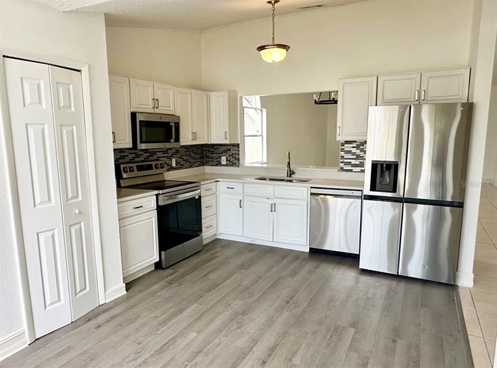 A kitchen features white cabinets, stainless steel appliances, a tiled backsplash, and wood-look flooring — 2784 FALLING TREE CIRCLE, ORLANDO, FL