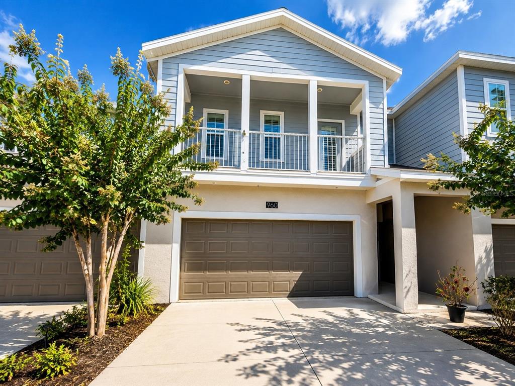 A two-story house exterior features a light blue upper level, a brown garage, and a balcony — 960 GRAND WILDMERE COVE, LONGWOOD, FL