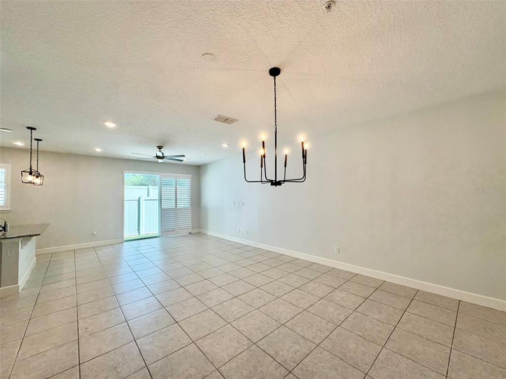 A spacious room features light-colored tile flooring, a black chandelier, and a sliding glass door — 960 GRAND WILDMERE COVE, LONGWOOD, FL