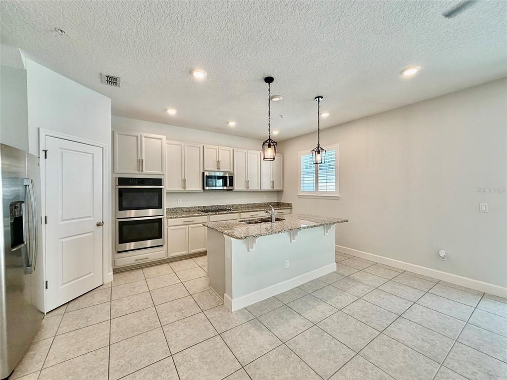 A kitchen features white cabinetry, granite countertops, a center island, and stainless steel appliances — 960 GRAND WILDMERE COVE, LONGWOOD, FL
