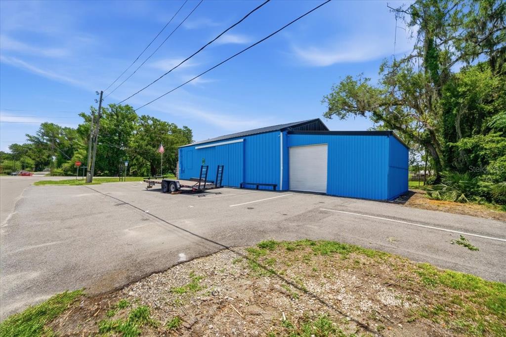 A bright blue metal warehouse building sits on an asphalt lot with a utility trailer — 490 SMITH STREET, BROOKSVILLE, FL