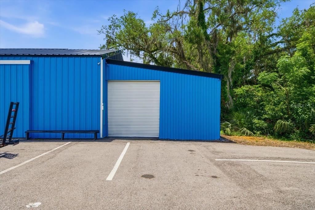 A blue metal building with a white roll-up door sits next to a paved parking lot — 490 SMITH STREET, BROOKSVILLE, FL