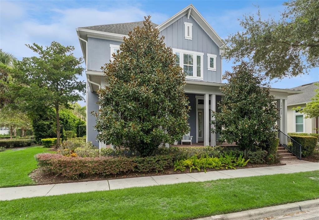 A two-story blue house with a front porch, large magnolia trees, and a landscaped yard — 13117 LESSING AVENUE, ORLANDO, FL
