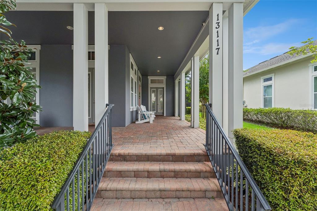 A covered brick porch with steps, a metal railing, and white columns leads to a doorway — 13117 LESSING AVENUE, ORLANDO, FL