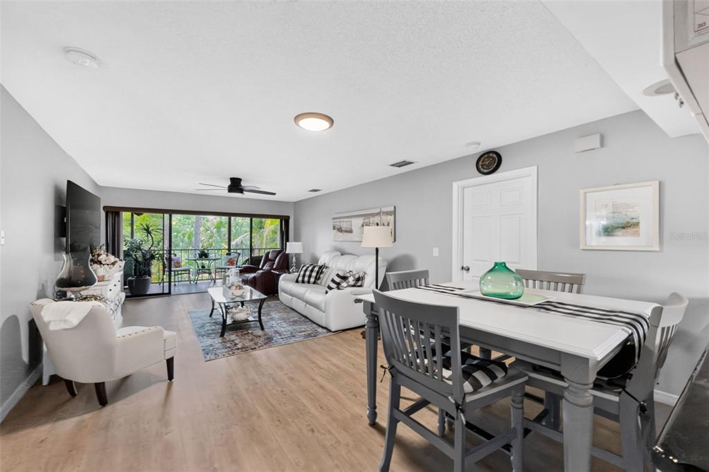 An open-concept living and dining area features light wood flooring, gray walls, and a balcony — 4260 PLACIDA ROAD UNIT 17D, ENGLEWOOD, FL