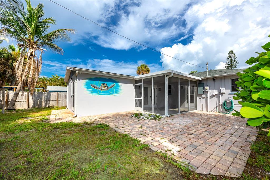 A backyard features a paved patio, a screened-in porch, and a turtle mural on the wall — 504 79TH AVENUE, ST PETE BEACH, FL