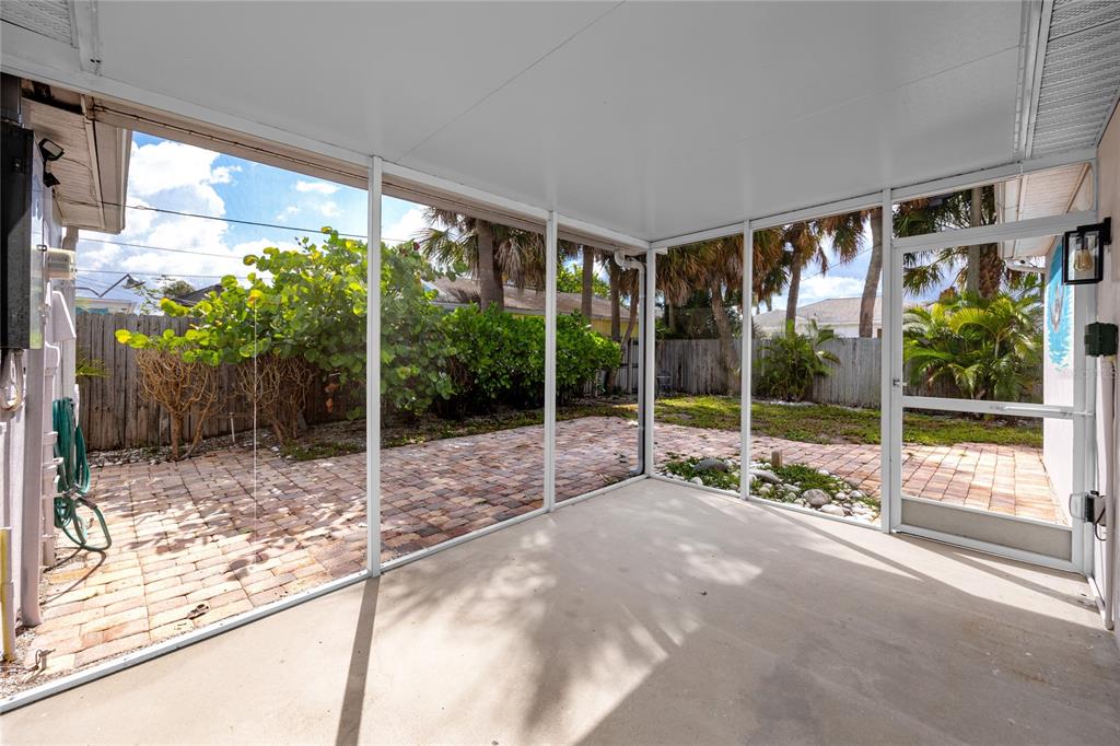 A screened-in patio with a concrete floor overlooks a brick-paved backyard with palm trees — 504 79TH AVENUE, ST PETE BEACH, FL