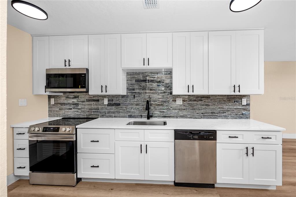 A kitchen features white cabinets, stainless steel appliances, and a gray tiled backsplash — 504 79TH AVENUE, ST PETE BEACH, FL