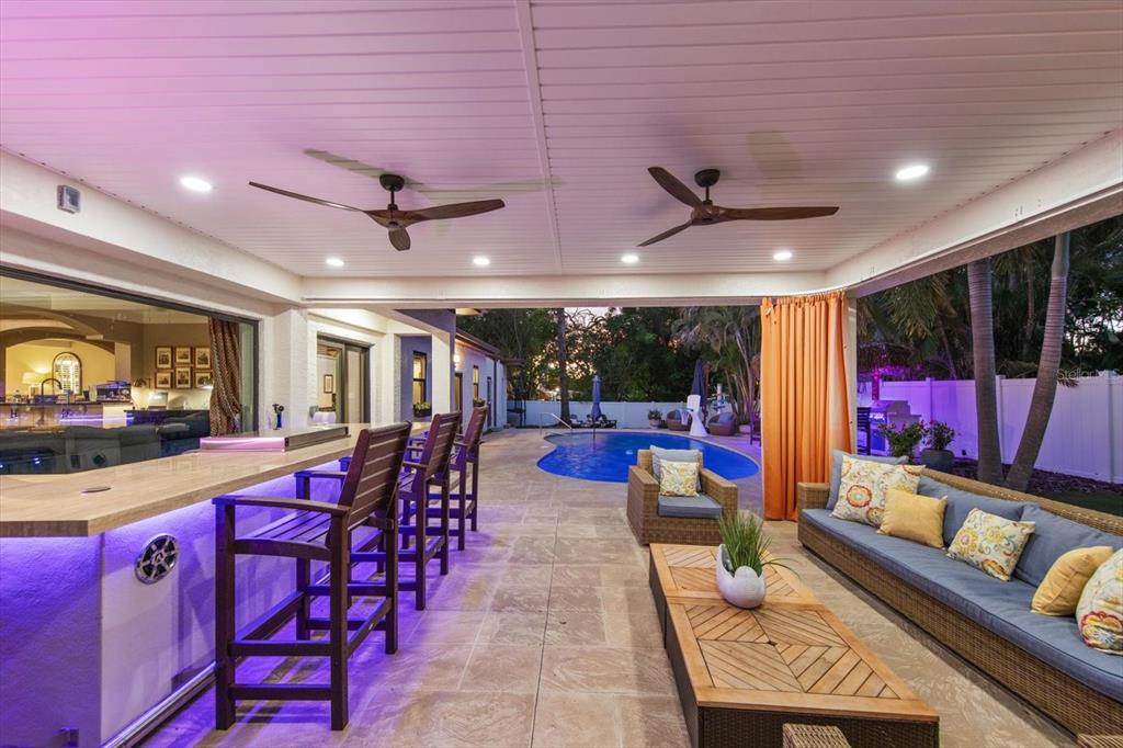 A covered outdoor patio features a bar, seating area, and a view of a swimming pool — 3005 SUNSET DRIVE, BELLEAIR BLUFFS, FL
