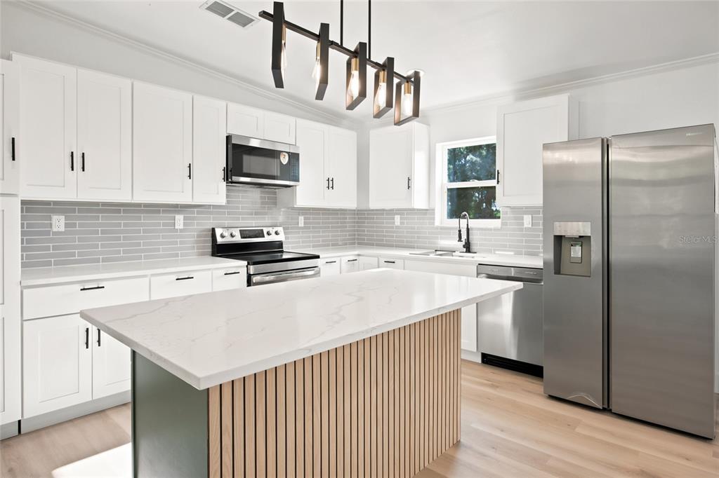 A modern kitchen features white cabinets, a slatted wood island, and stainless steel appliances — 2625 SE 140TH PLACE, SUMMERFIELD, FL