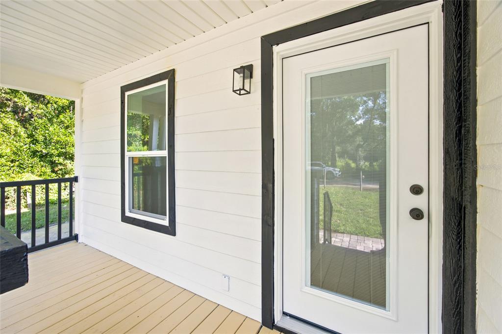 A white front door and window with black trim on a covered wooden porch — 2625 SE 140TH PLACE, SUMMERFIELD, FL