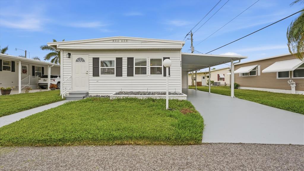 A white mobile home with black shutters and a covered carport under a blue sky — 4908 5TH A STREET E, BRADENTON, FL