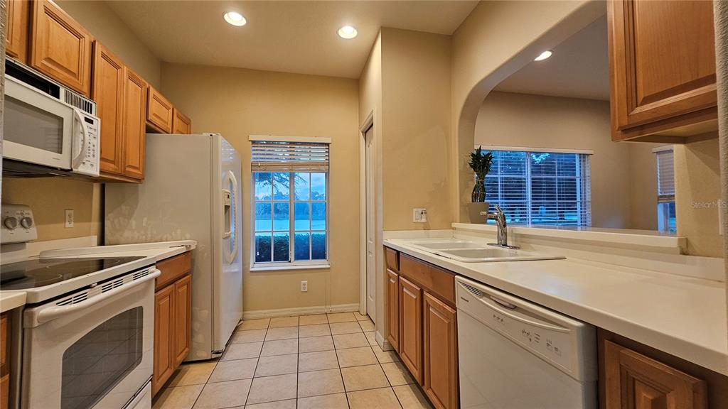 A kitchen with wood cabinets, white appliances, tile flooring, and a window overlooking a lake — 220 CAPE HARBOUR LOOP UNIT 108, BRADENTON, FL