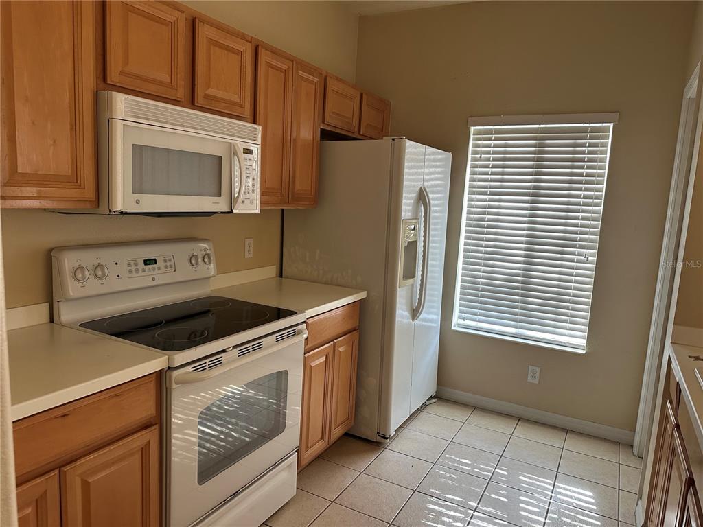 A kitchen features light wood cabinets, white appliances, a tiled floor, and a window with blinds — 220 CAPE HARBOUR LOOP UNIT 108, BRADENTON, FL