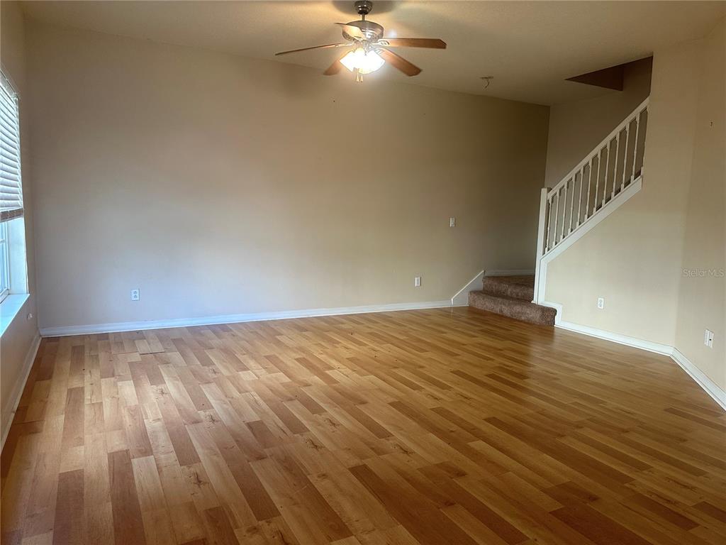 An empty living room features wood-look flooring, a ceiling fan, and a staircase with railings — 220 CAPE HARBOUR LOOP UNIT 108, BRADENTON, FL