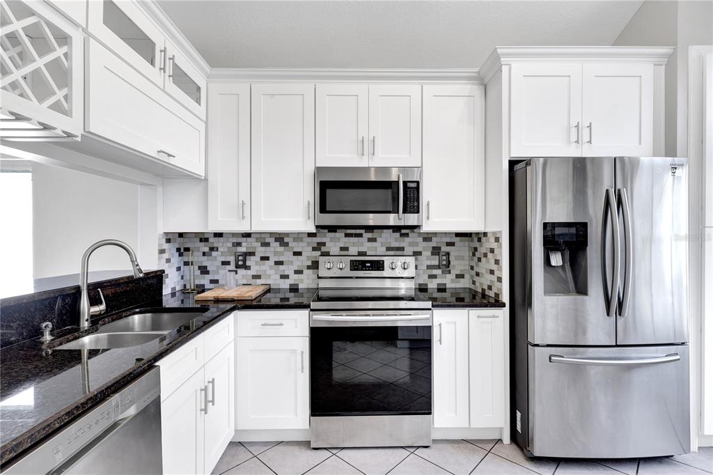 A kitchen features white cabinets, stainless steel appliances, a mosaic tile backsplash, and dark countertops — 789 HEATHER GLEN CIRCLE, LAKE MARY, FL