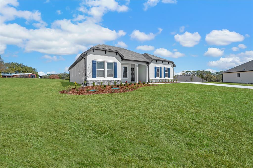 A single-story house with white stucco walls, blue shutters, and a stone-accented base — 3840 SADDLE HILL TRAIL, FRUITLAND PARK, FL