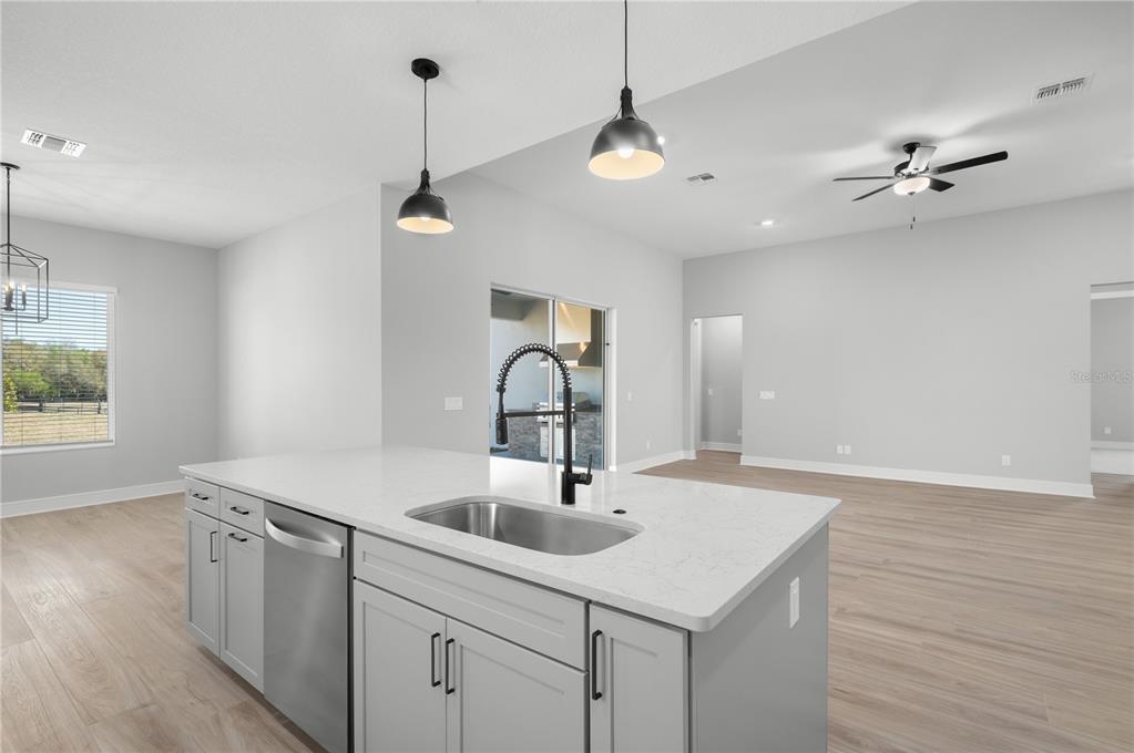 A modern kitchen features white cabinetry, a large gray island, stainless appliances, and light flooring — 3840 SADDLE HILL TRAIL, FRUITLAND PARK, FL