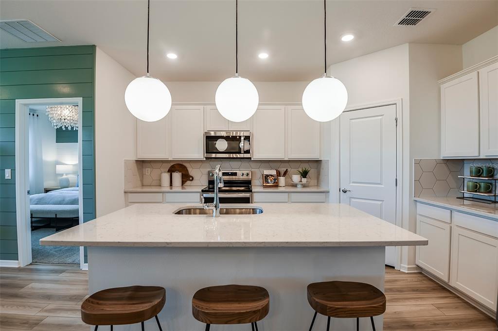 A kitchen features a white quartz island, three globe pendant lights, and white cabinetry — 14818 SUNBEAM STREET, PARRISH, FL