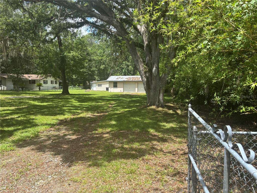 A grassy backyard features large oak trees, a chain-link fence, and a detached garage — 7546 SONIA DRIVE, JACKSONVILLE, FL