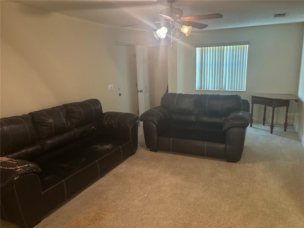 A living room features two dark leather sofas, beige carpeting, and a ceiling fan — 7546 SONIA DRIVE, JACKSONVILLE, FL