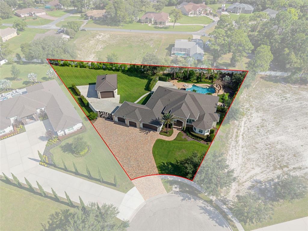 An aerial view shows a house with a pool, detached garage, and large paved driveway — 533 STORYBOOK LANE, SPRING HILL, FL