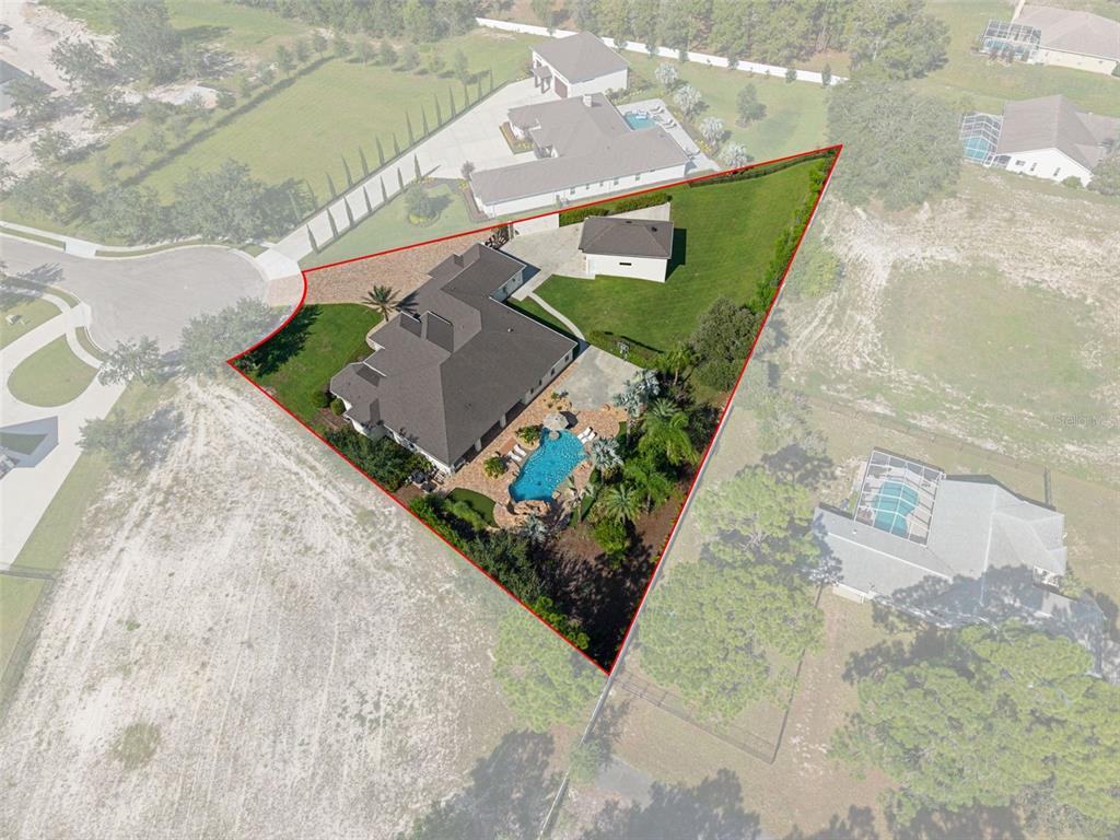 An aerial view shows a house with a pool and detached garage on a triangular lot — 533 STORYBOOK LANE, SPRING HILL, FL