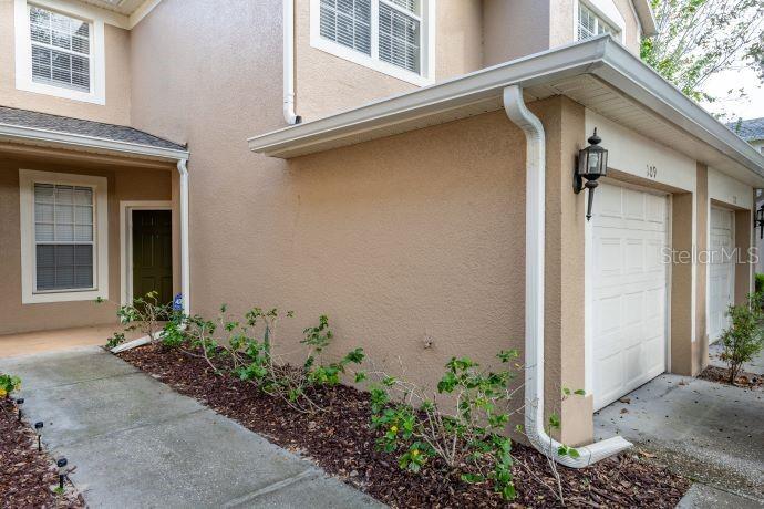 The exterior of a tan townhouse features a garage, a front door, and small shrubs — 2679 METRO SEVILLA DRIVE UNIT 109, ORLANDO, FL