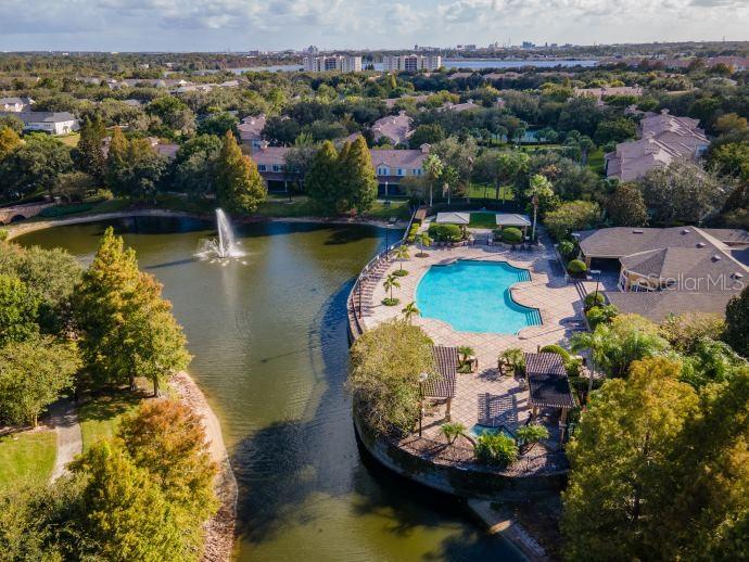 An aerial view shows a community swimming pool and fountain situated beside a lake — 2679 METRO SEVILLA DRIVE UNIT 109, ORLANDO, FL