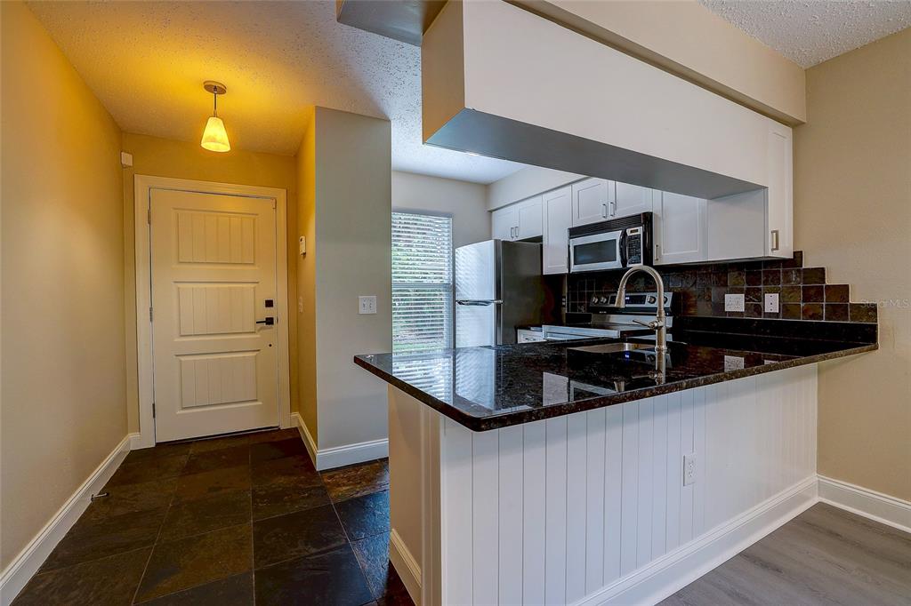 A kitchen with dark granite countertops and white cabinets overlooks a tiled entryway with a door — 4625 SUMMERWIND DRIVE UNIT 13, SARASOTA, FL