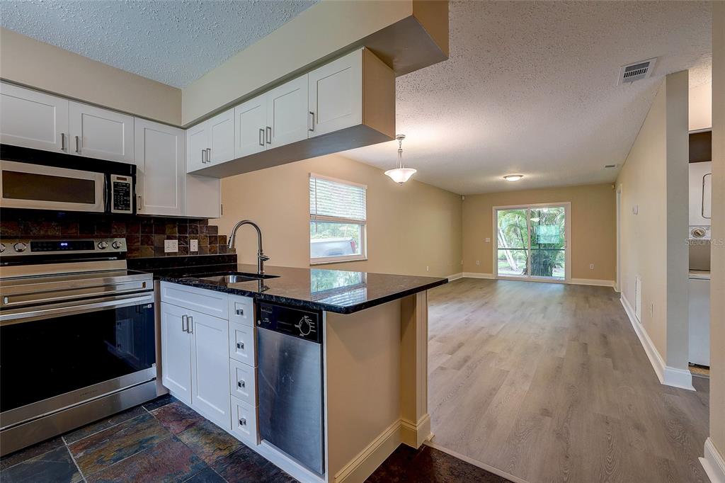 A kitchen with white cabinets and black countertops opens into a living area with wood flooring — 4625 SUMMERWIND DRIVE UNIT 13, SARASOTA, FL