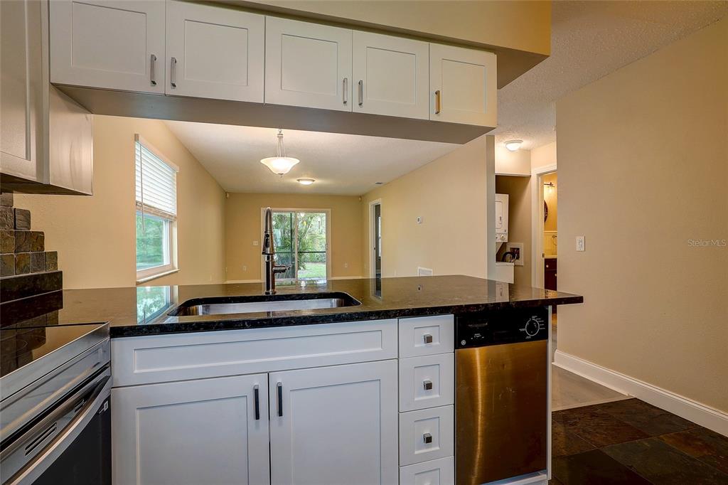 A kitchen with white cabinets, dark countertops, and a stainless steel dishwasher overlooks a living area — 4625 SUMMERWIND DRIVE UNIT 13, SARASOTA, FL