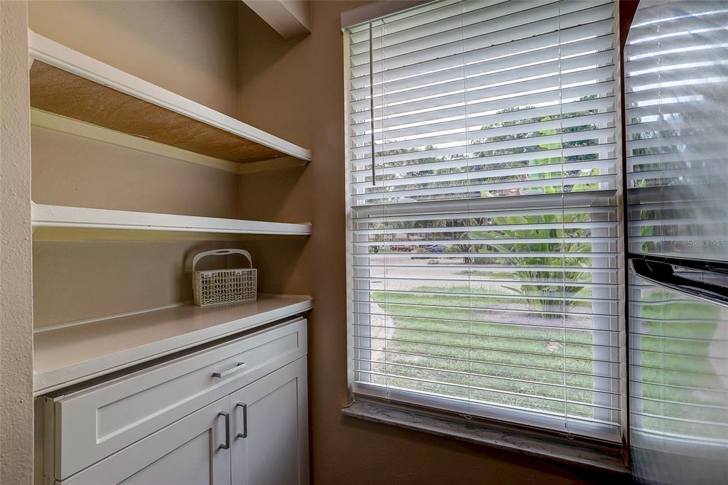 A kitchen nook features white cabinets, open shelving, and a window with horizontal blinds — 4625 SUMMERWIND DRIVE UNIT 13, SARASOTA, FL