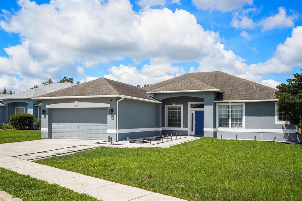 A single-story gray house features a two-car garage, a blue front door, and a lawn — 417 WILDFLOWER RD, DAVENPORT, FL