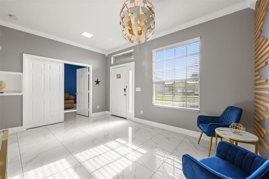 A bright entryway features white marble-look tile floors, gray walls, blue chairs, and a modern chandelier — 417 WILDFLOWER RD, DAVENPORT, FL