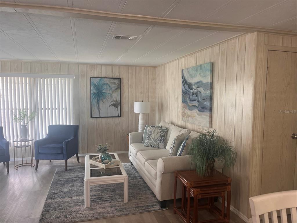 A living room features light wood-paneled walls, a white sofa, and a large starfish wall decoration — 5316 53RD AVENUE E UNIT O12, BRADENTON, FL
