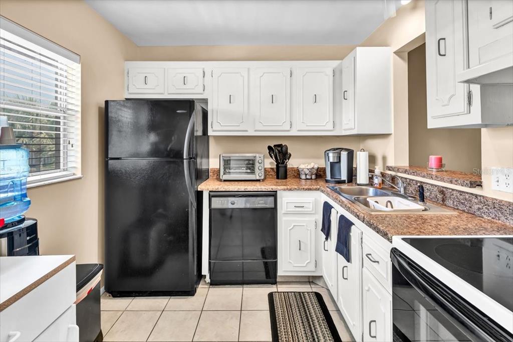 A kitchen features white cabinets, granite countertops, a black refrigerator, and a black dishwasher — 11485 OAKHURST ROAD UNIT 200-321, LARGO, FL