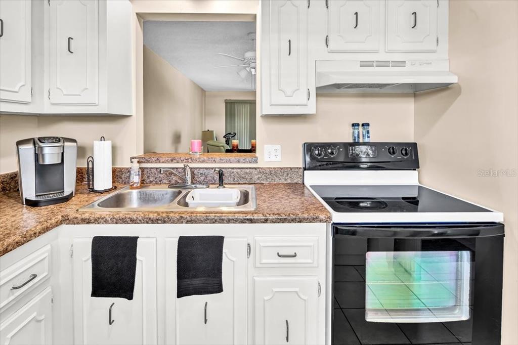 A kitchen features white cabinets, a granite countertop, a double sink, and a black stove — 11485 OAKHURST ROAD UNIT 200-321, LARGO, FL